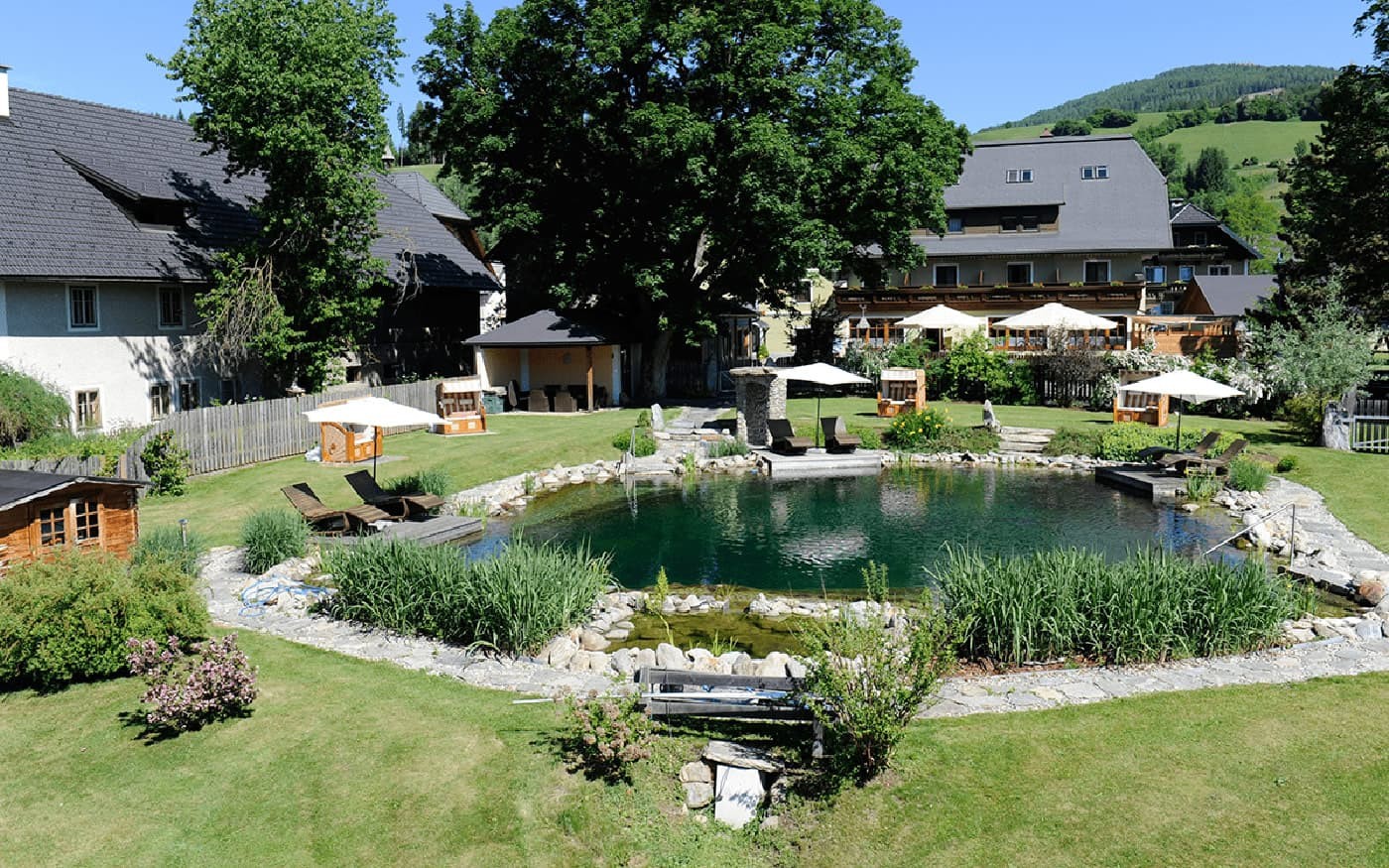 Grüner Garten mit kleinem Naturteich und umgeben von traditionellen Gebäuden