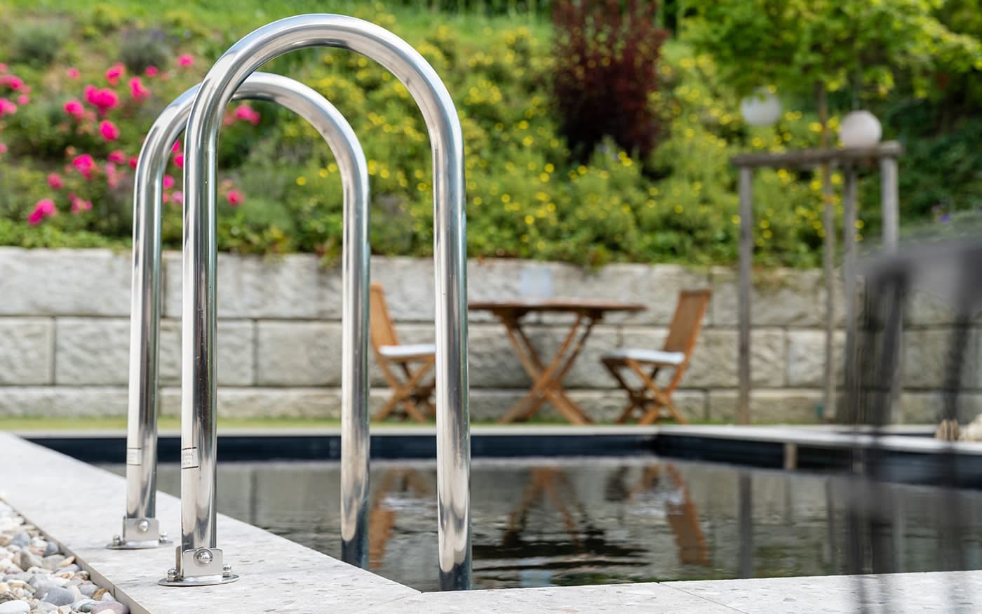 Poolleiter mit Blick auf Tisch und Stühle in einem blühenden Garten